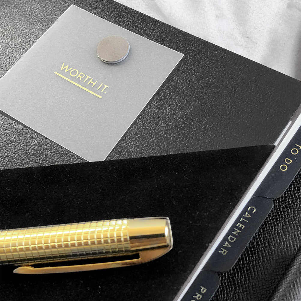A black velvet suede like planner folder inside a luxury a5 6 ring agenda by Louis Vuitton in black epi leather with a gold and black stationery pen sitting on top. A frosted planner card is fixed on the folder with a magnetic planner clip in taupe.