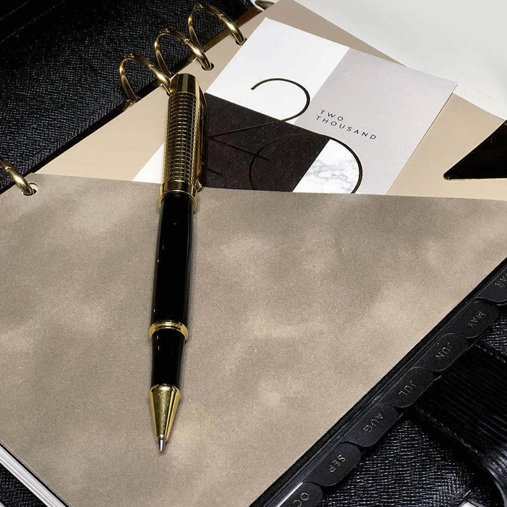 A taupe velvet suede like planner folder inside a luxury a5 6 ring agenda by Louis Vuitton in black epi leather with a gold and black stationery pen sitting on top